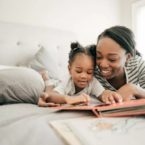 mother and toddler lay on the bed together reading a book