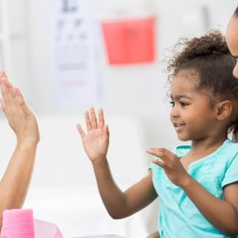 Vaccine success! A child giving a doctor a high five while sitting on her mom's lap