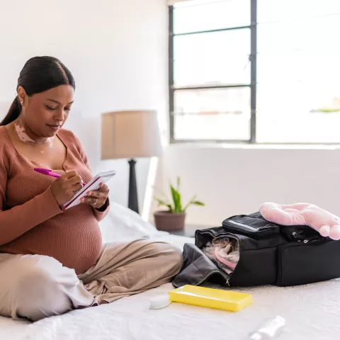 oung pregnant packing the baby clothes and maternity items on backpack at home 