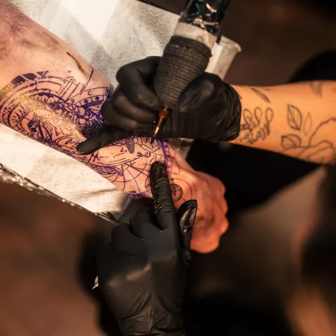 Tattoo artist inking intricate design on client's arm in a studio setting