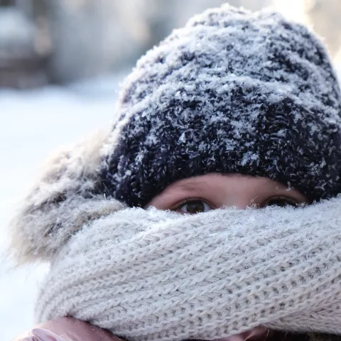 Young girl hiding her face with knitted bulky scarf during winter frost snowfall outdoors.
