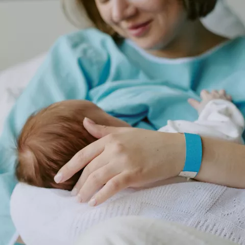 Mother Breastfeeding Newborn Baby in Hospital Room