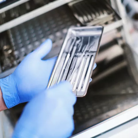 Unrecognizable male dental technician picking dental instruments from a sterilizer for a basic dental set up.