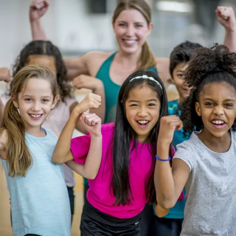 A group of elementary school students are posing with their teacher during gym class. 