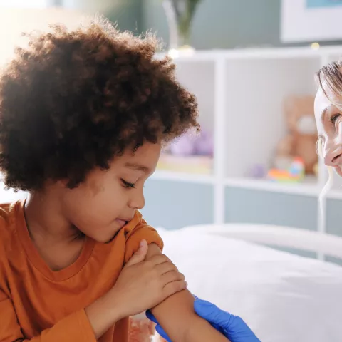 A parent and child sit with a smiling doctor following a vaccination appointment.