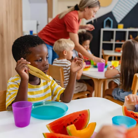 Preschool children sitting at a table eating fresh watermelon slices during snack time