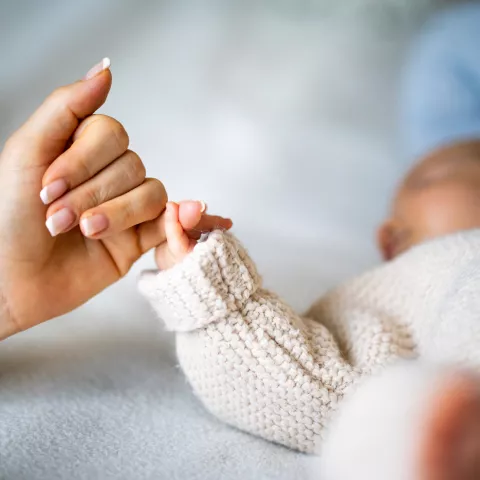 Close-up of mother's hand holding newborn baby's hand.