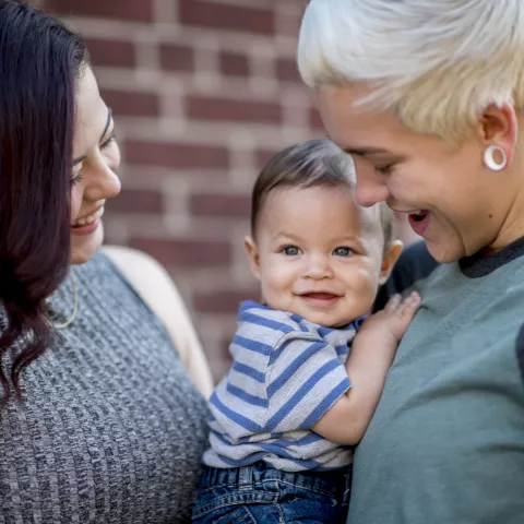 Young same sex couple adoringly smile at their baby boy