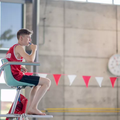 A lifeguard sits attentively at an indoor swimming pool, ensuring safety for swimmers. 