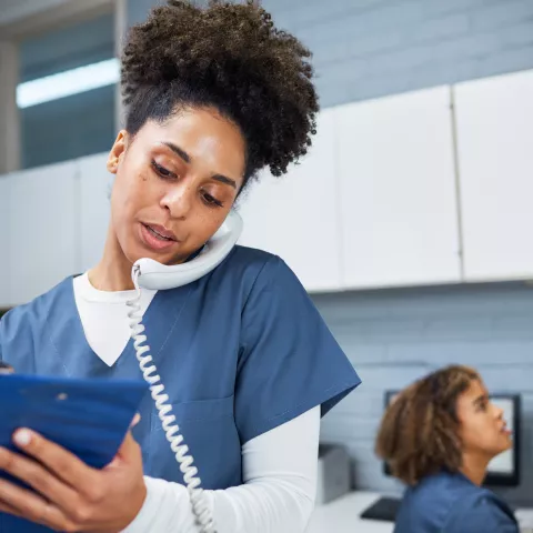 Female Healthcare Worker Taking Notes While Using a Phone in a Modern Medical Office
