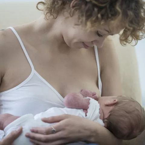 A young adult mother is breastfeeding her newborn baby.