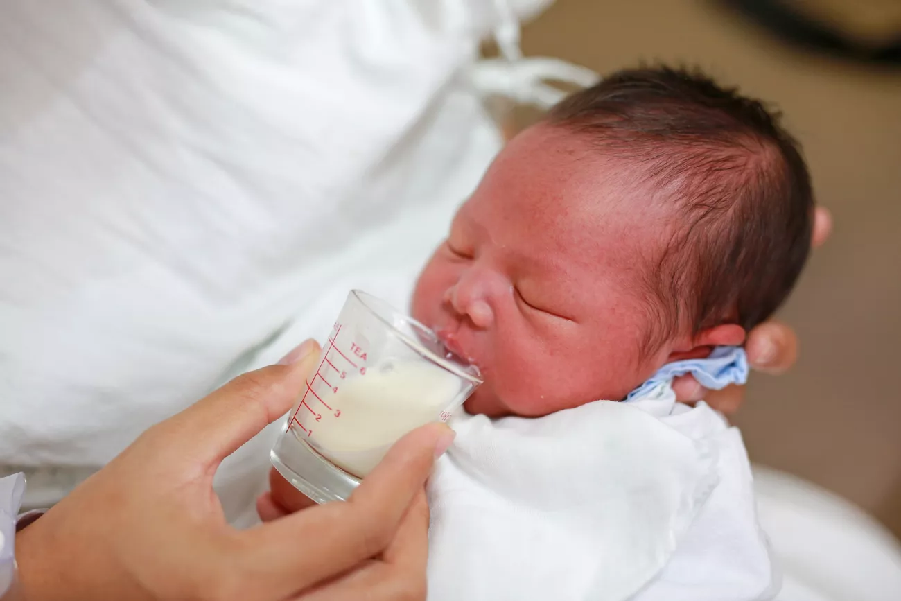 A baby being fed milk from a measuring cup.