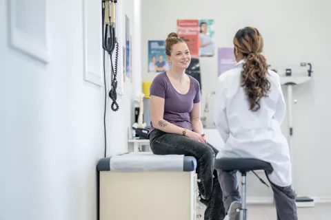 A young woman sits up on an exam table during a medical appointment