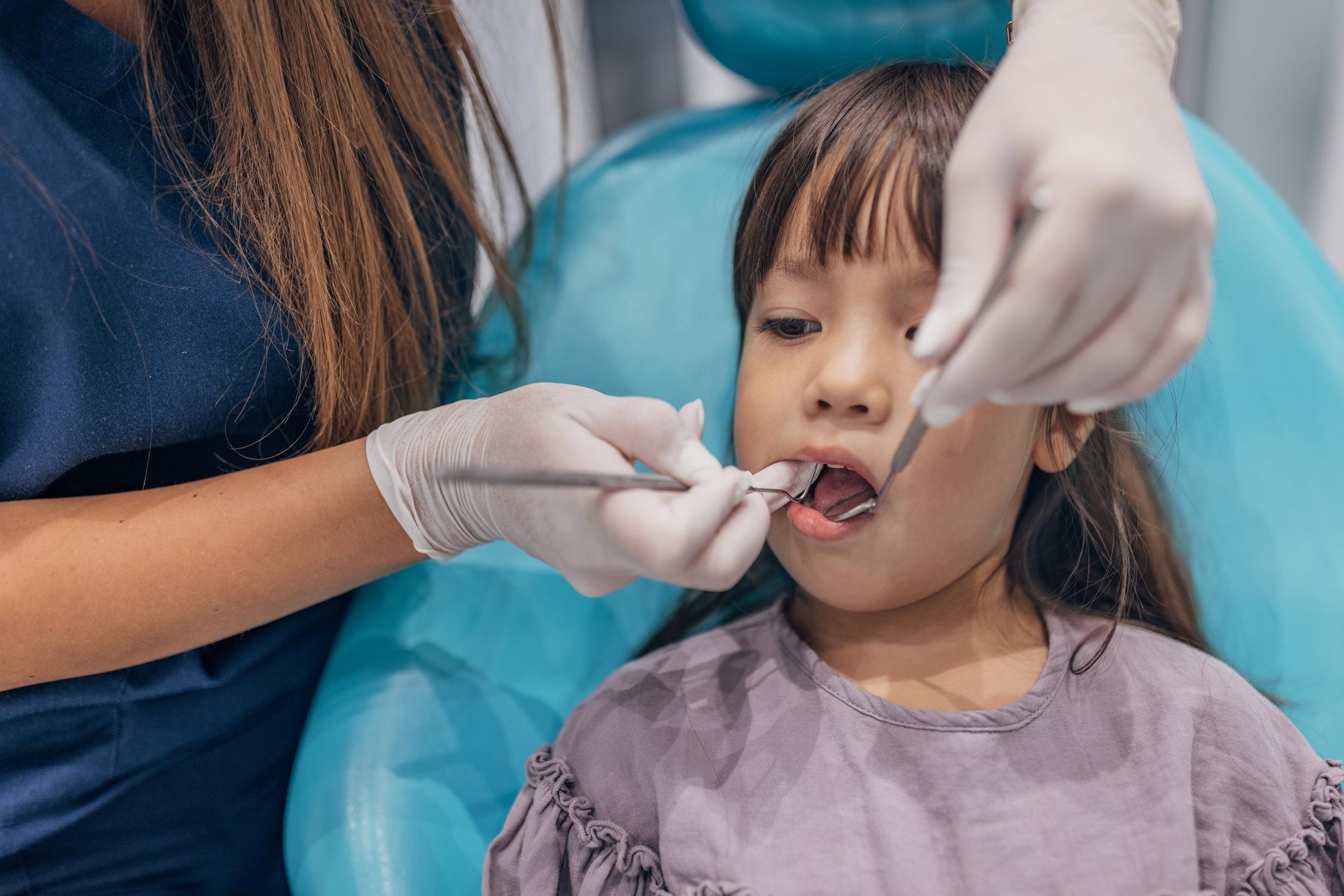 Female dentist examining her little girl patient teeth in dentist's office.