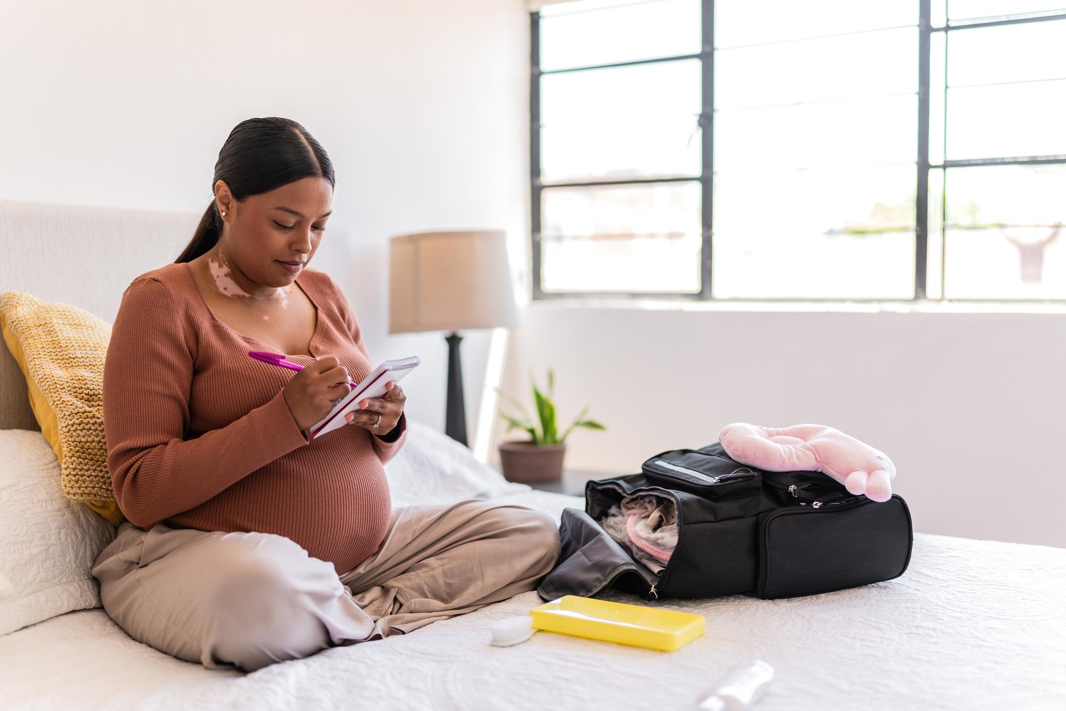 oung pregnant packing the baby clothes and maternity items on backpack at home 
