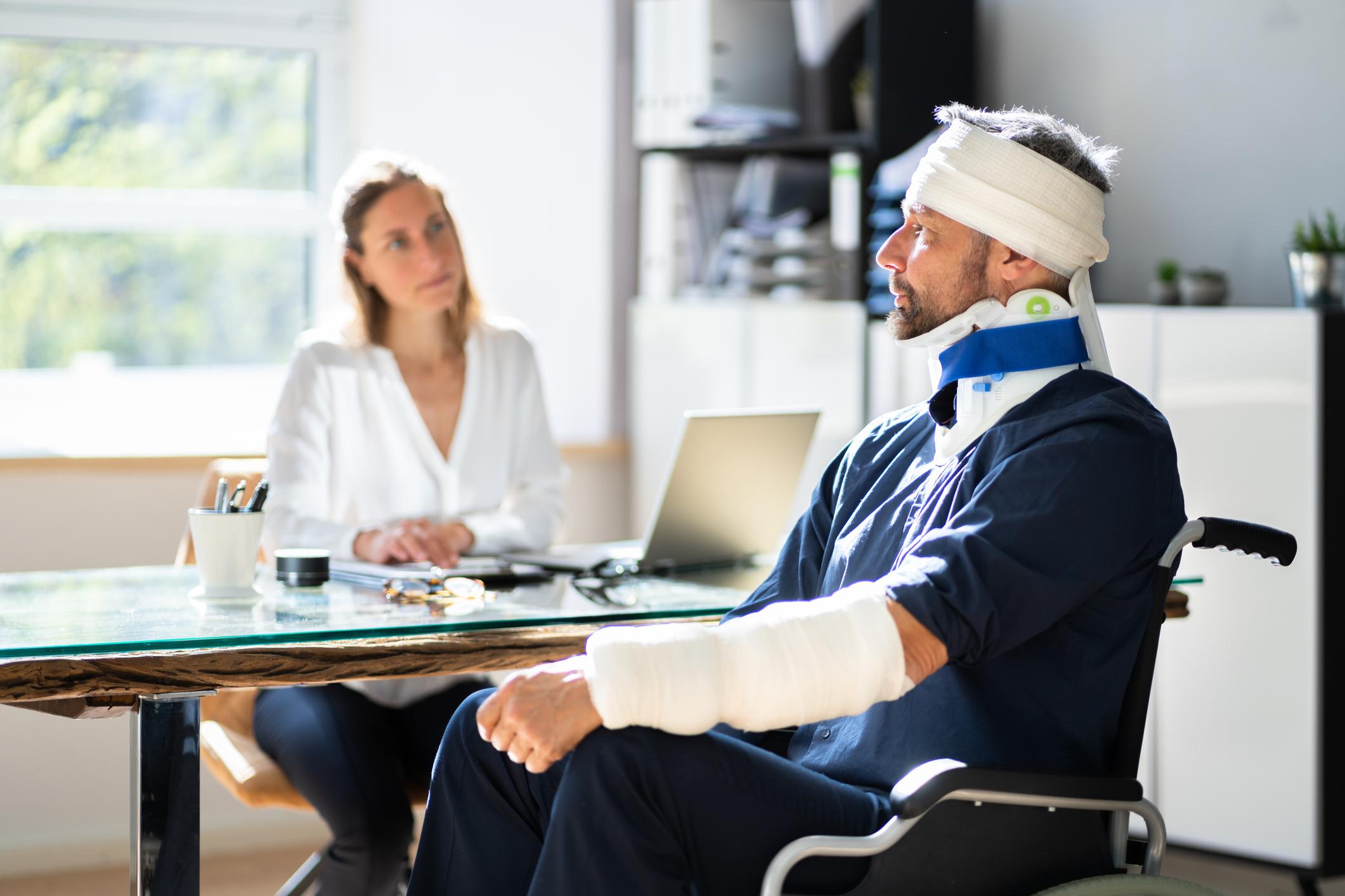 Injured man in casts and head bandages and neck brace talking to doctor