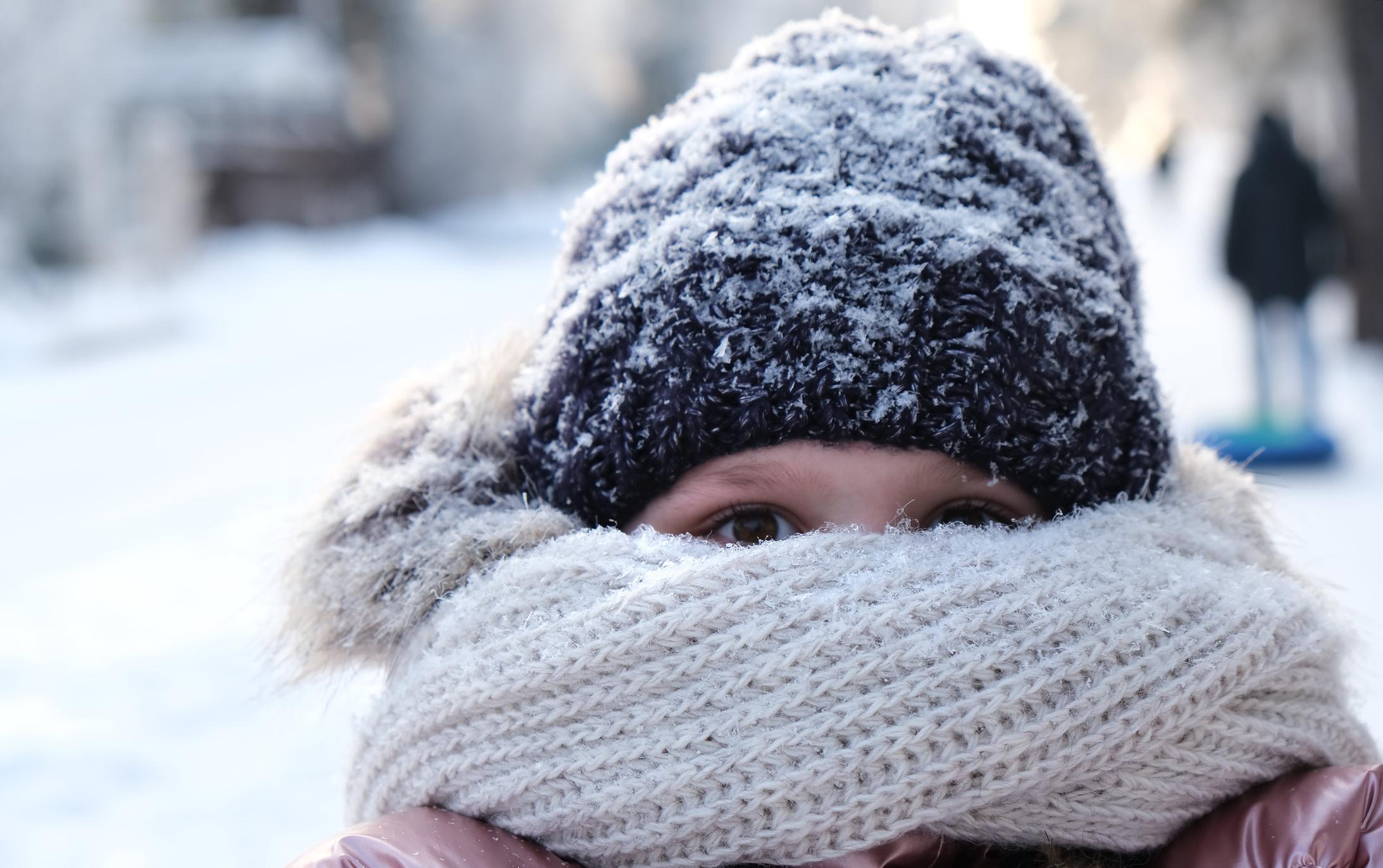 Young girl hiding her face with knitted bulky scarf during winter frost snowfall outdoors.