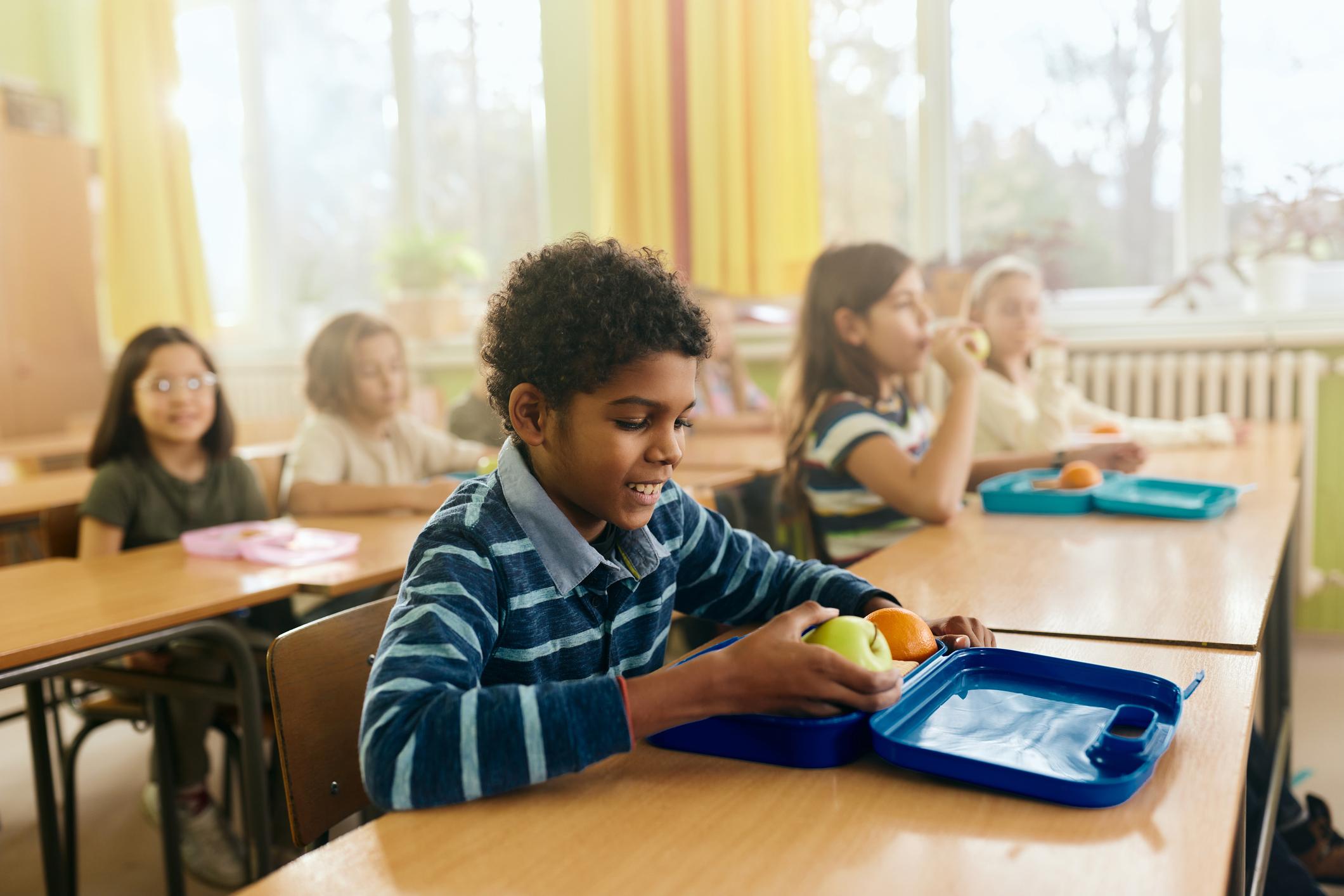 Happy black boy having fruit for snack during a break in the classroom