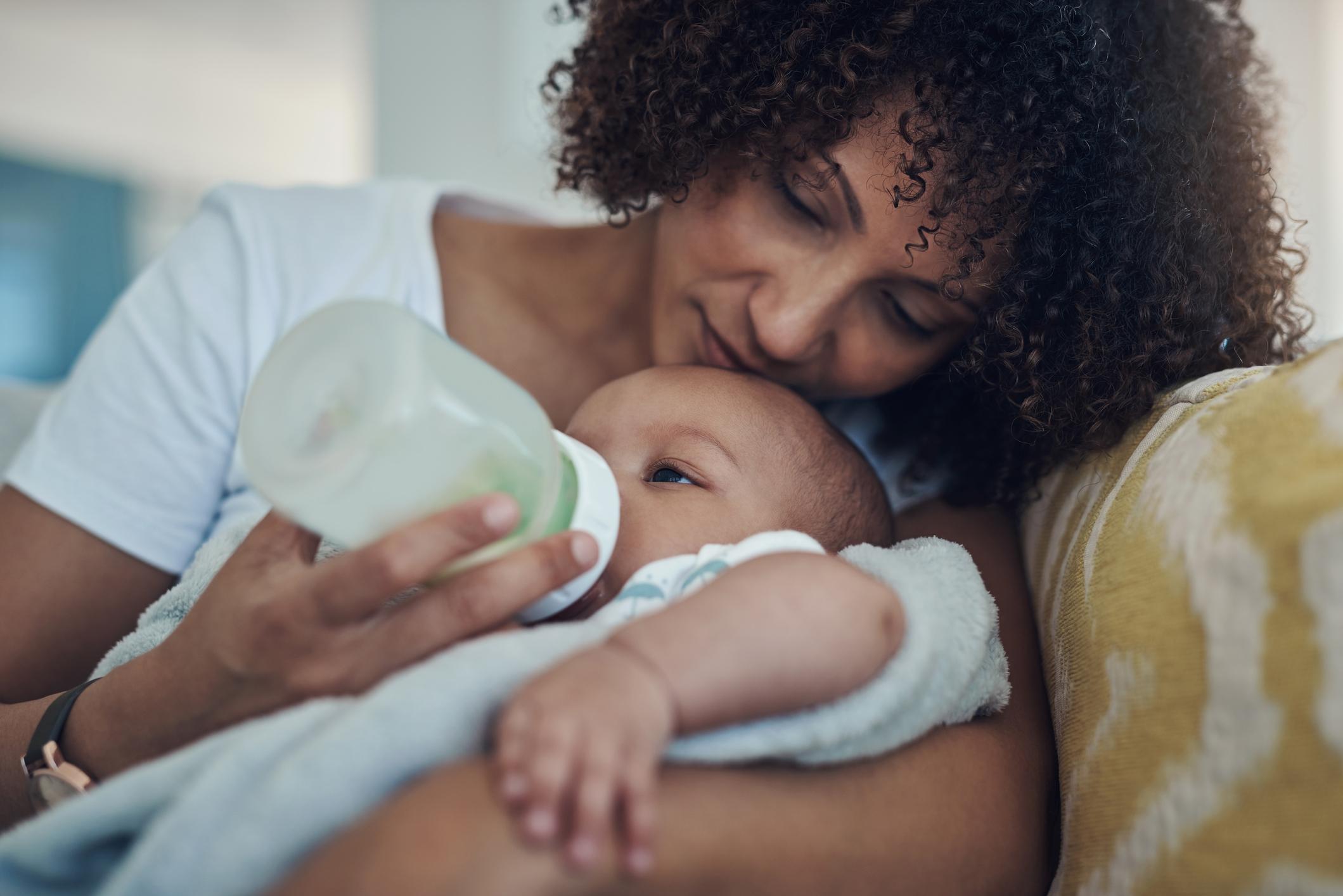 dorable baby girl being bottle fed by her mother on the sofa