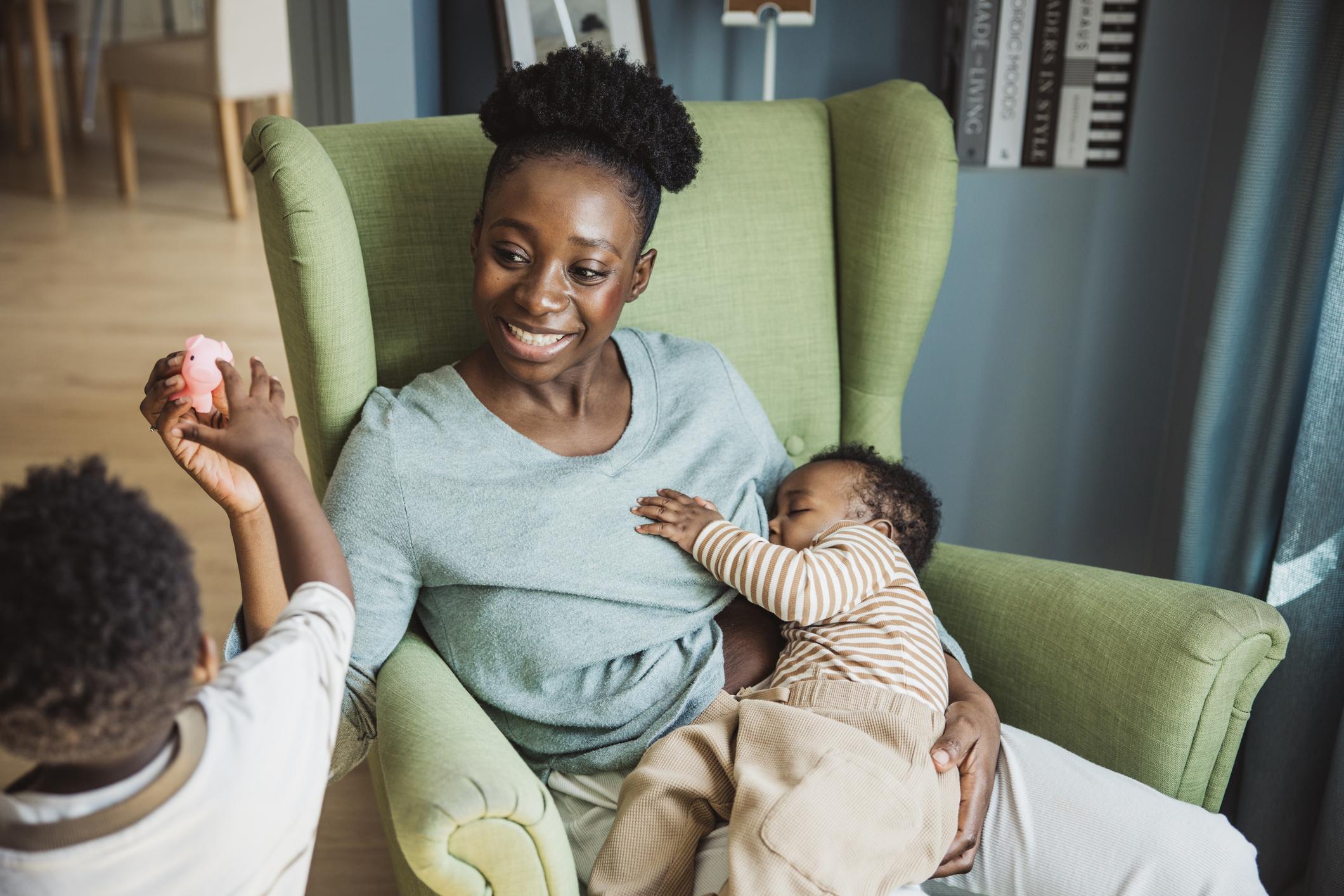 Young mother breastfeeding baby while playing with toddler