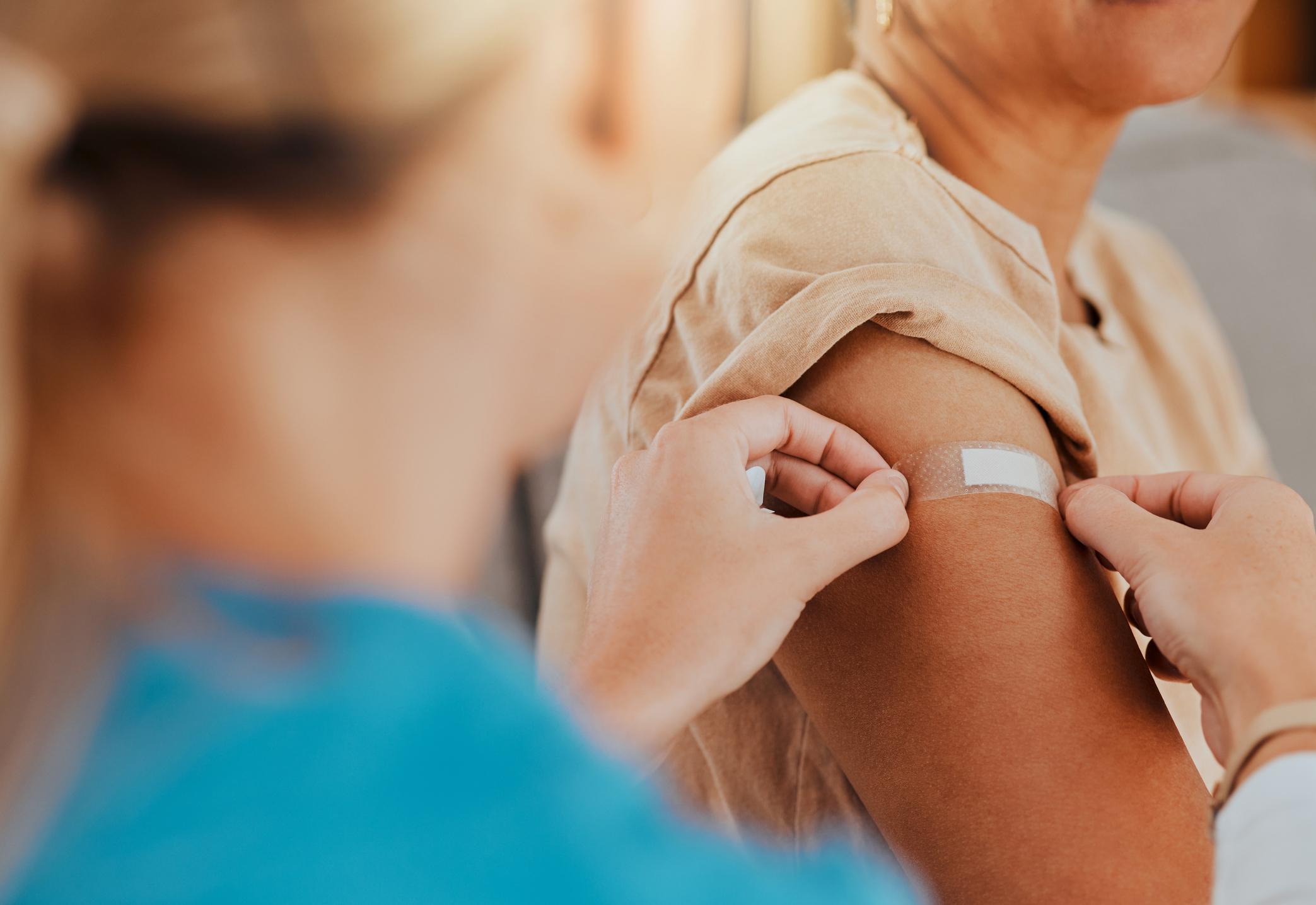 Someone getting a vaccine from a nurse, arm on bandaid