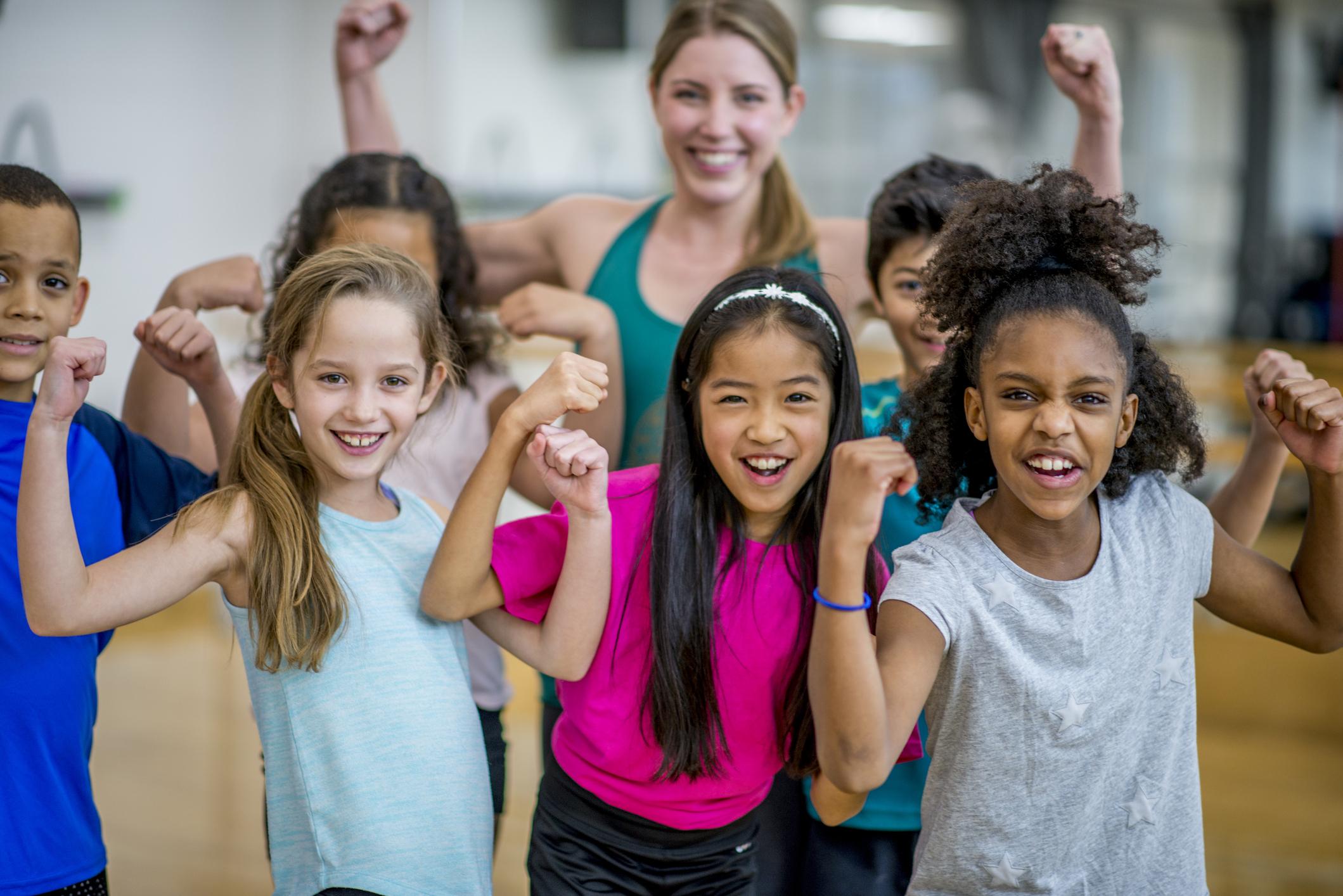 A group of elementary school students are posing with their teacher during gym class. 