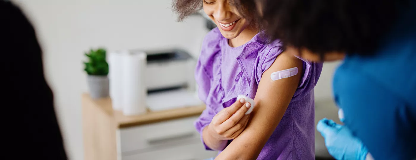 A teen girl receiving a vaccination from a nurse.
