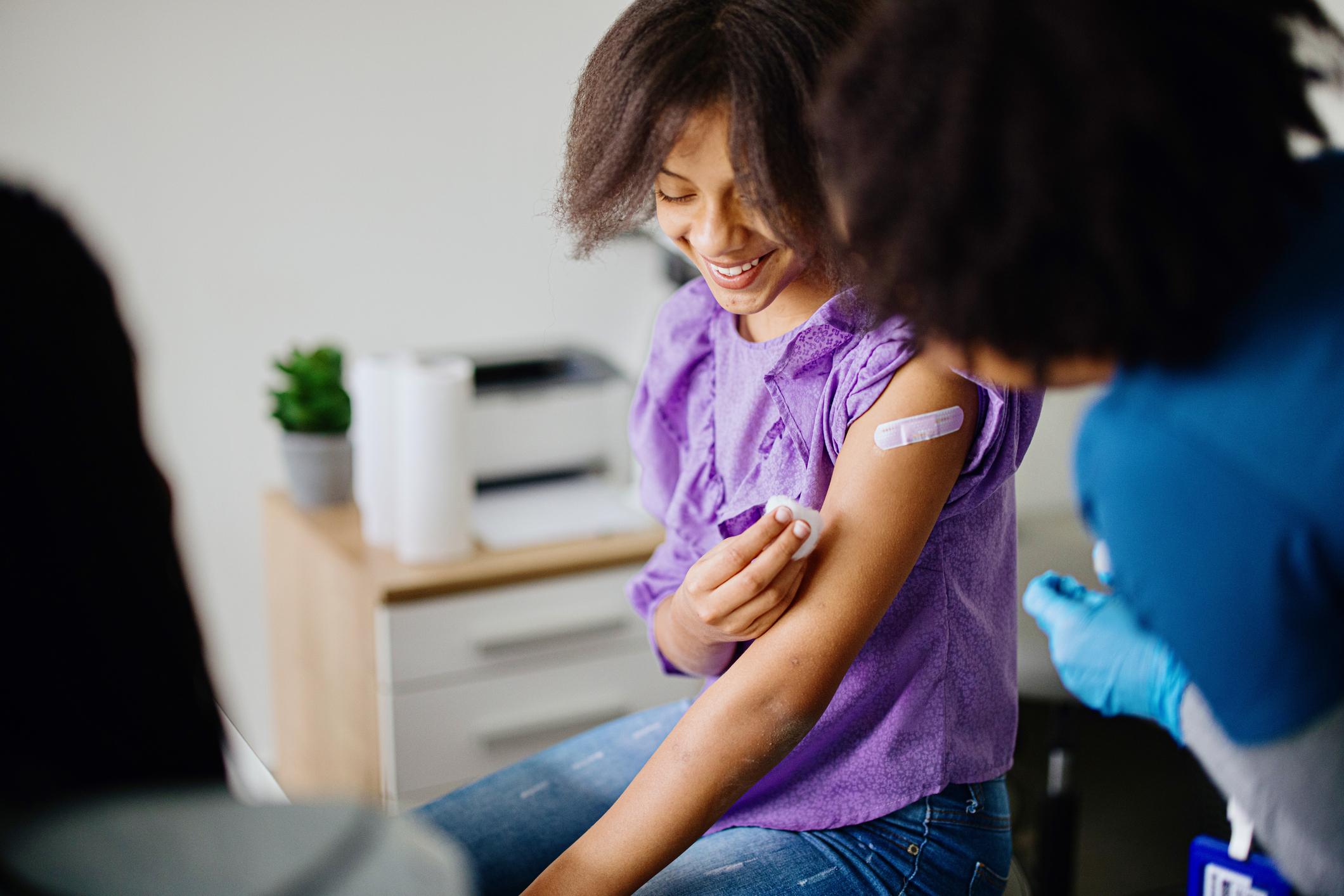 A teen girl receiving a vaccination from a nurse.