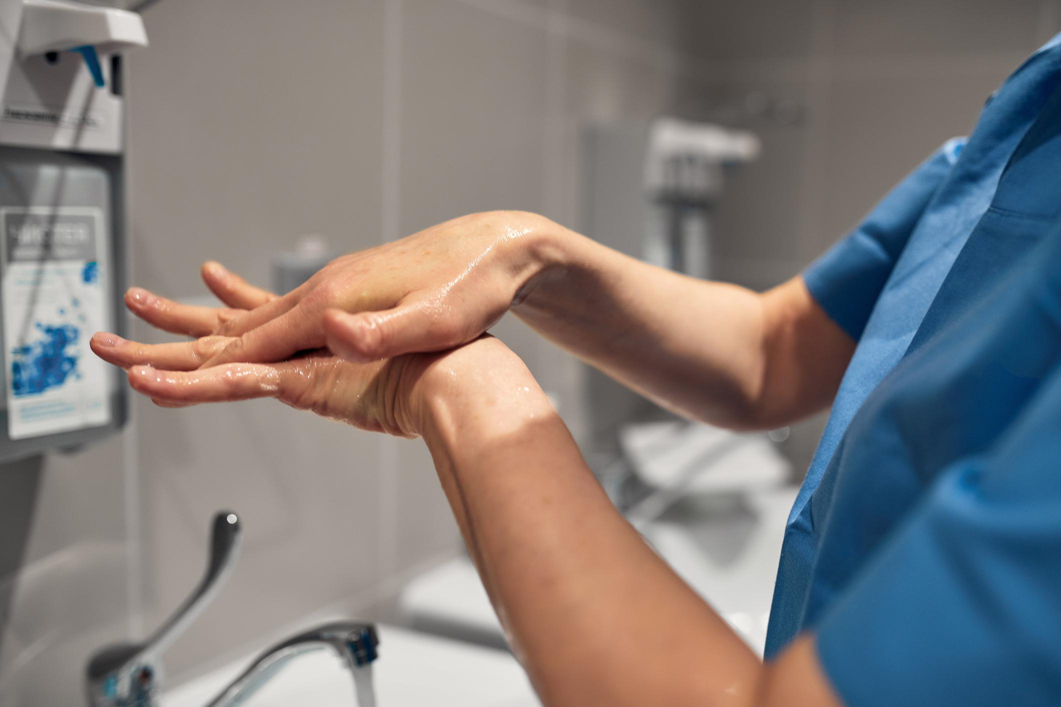 Close-up of a PSW washing his hands using a disinfectant dispenser - stock photo