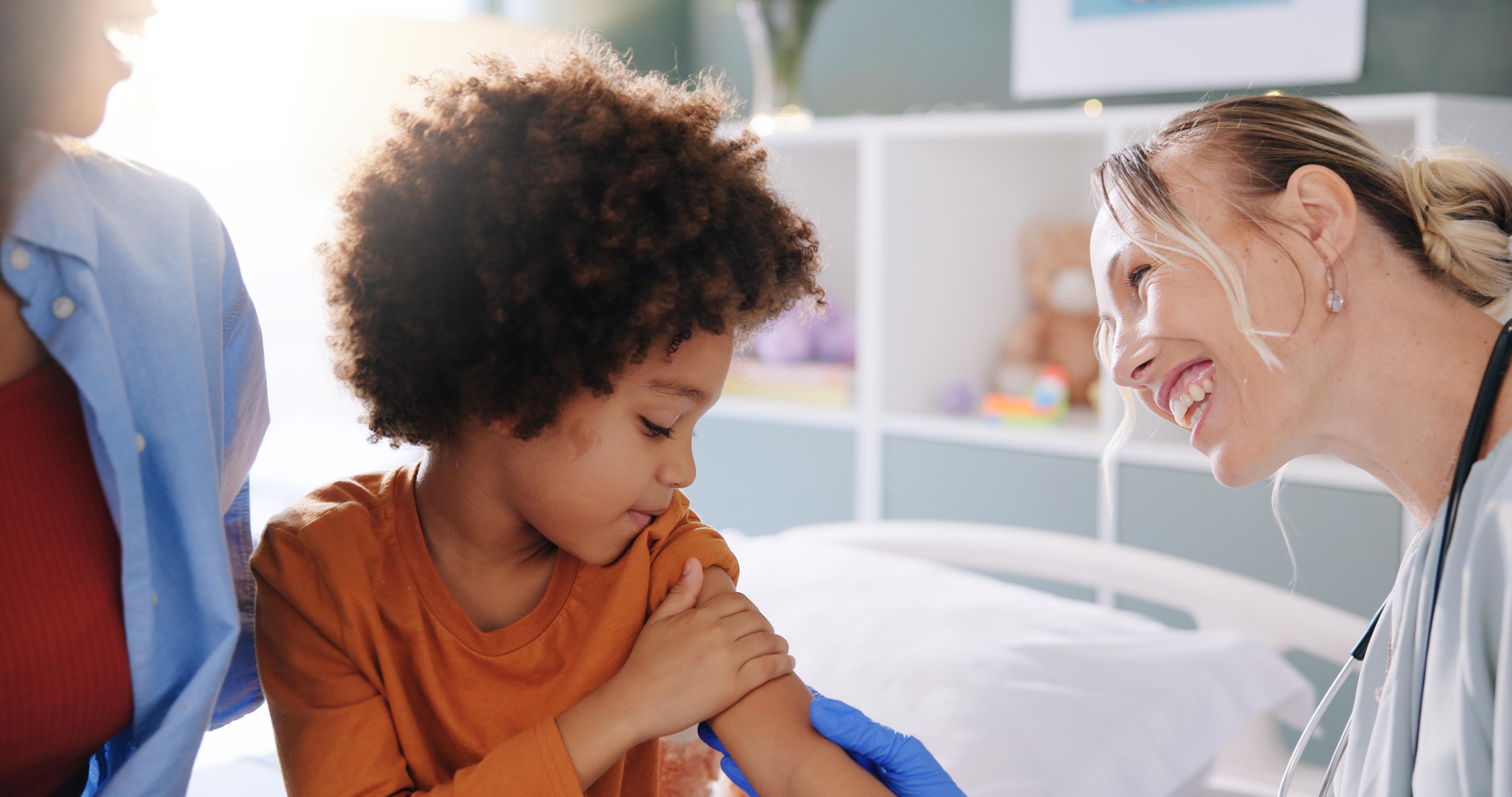 A parent and child sit with a smiling doctor following a vaccination appointment.