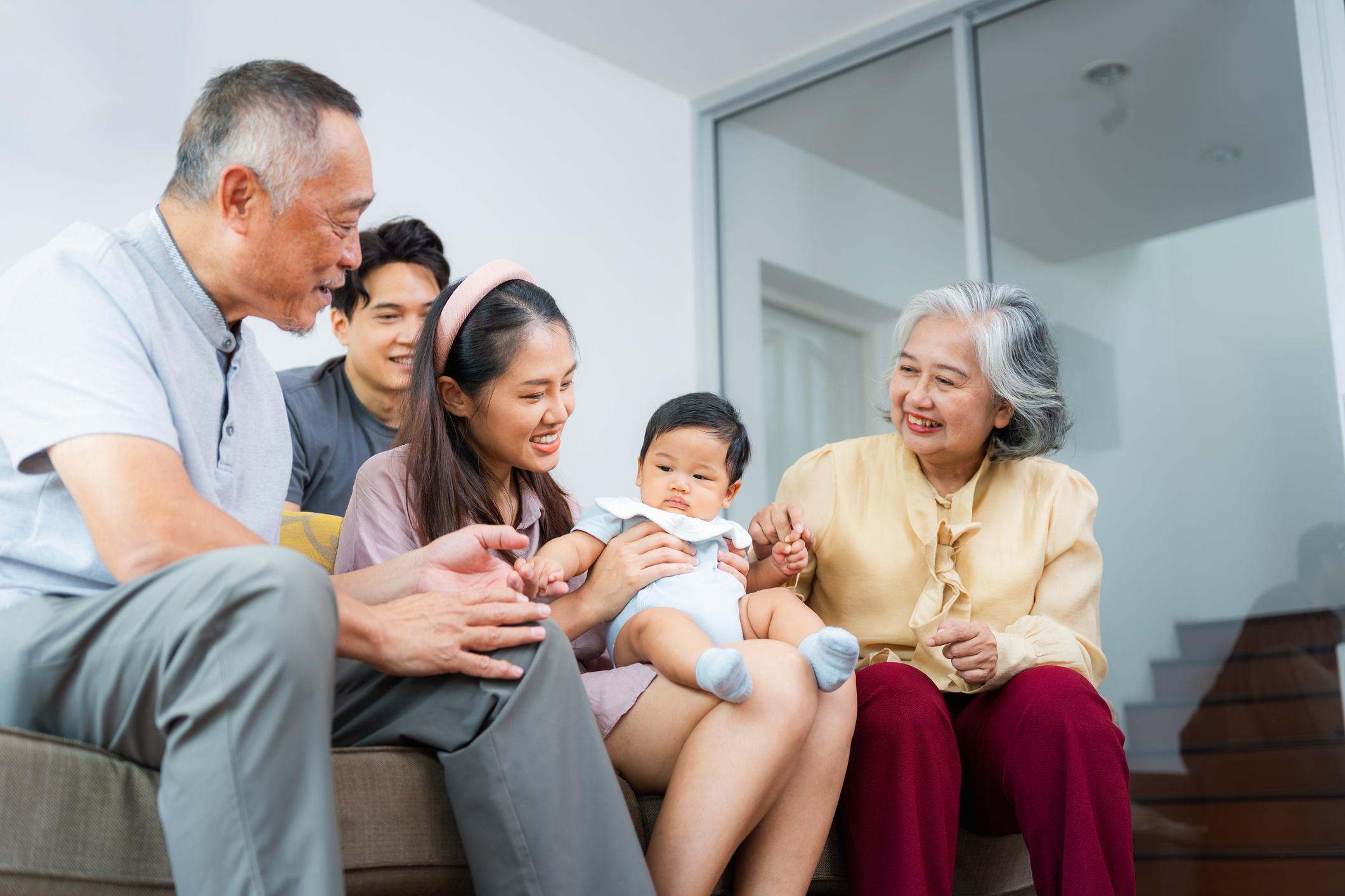 Cheerful Asian Grandparents, Parents, and Child Relaxing Together on Couch,