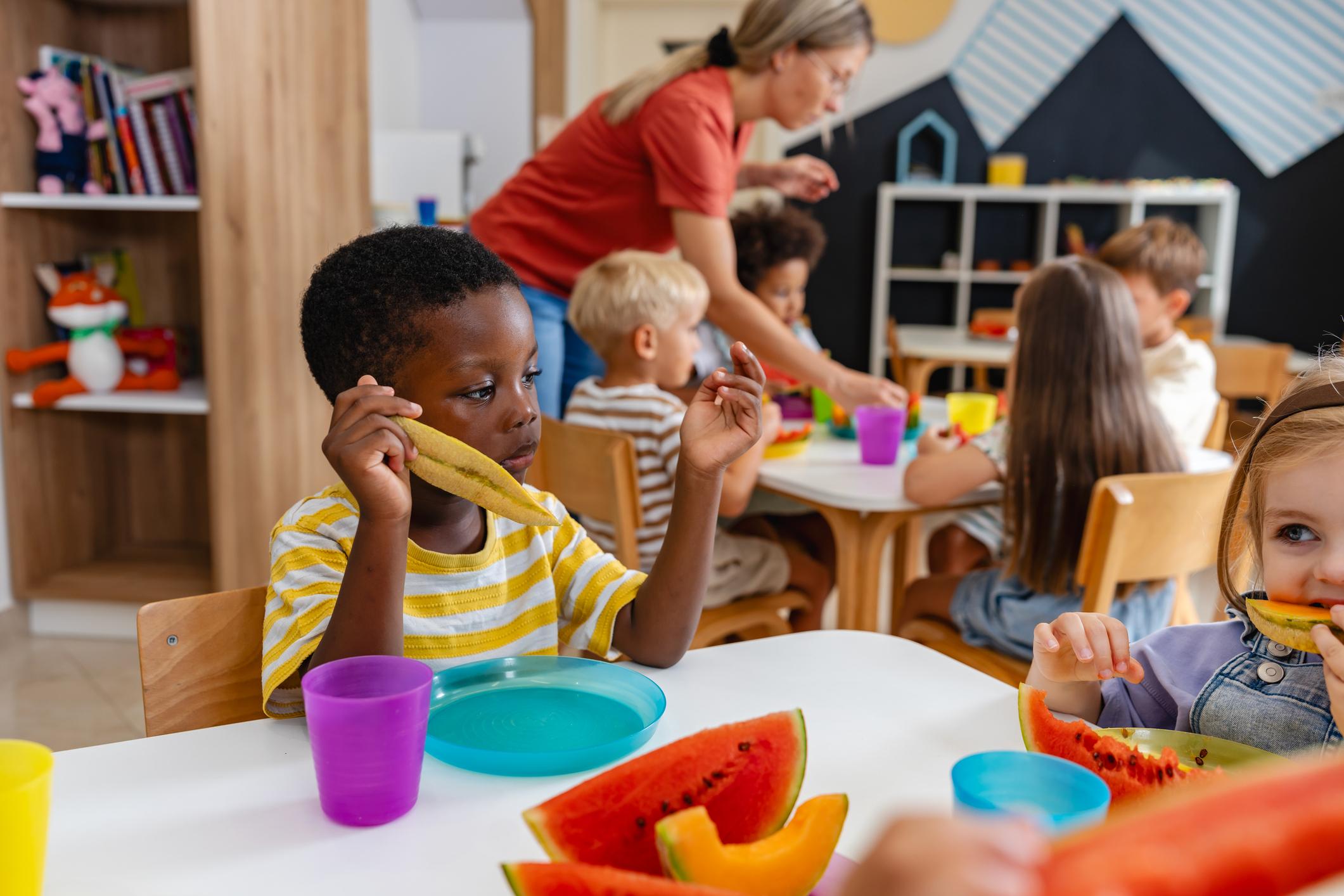 Preschool children sitting at a table eating fresh watermelon slices during snack time