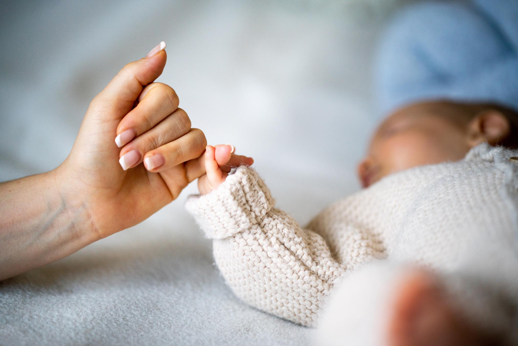 Close-up of mother's hand holding newborn baby's hand.