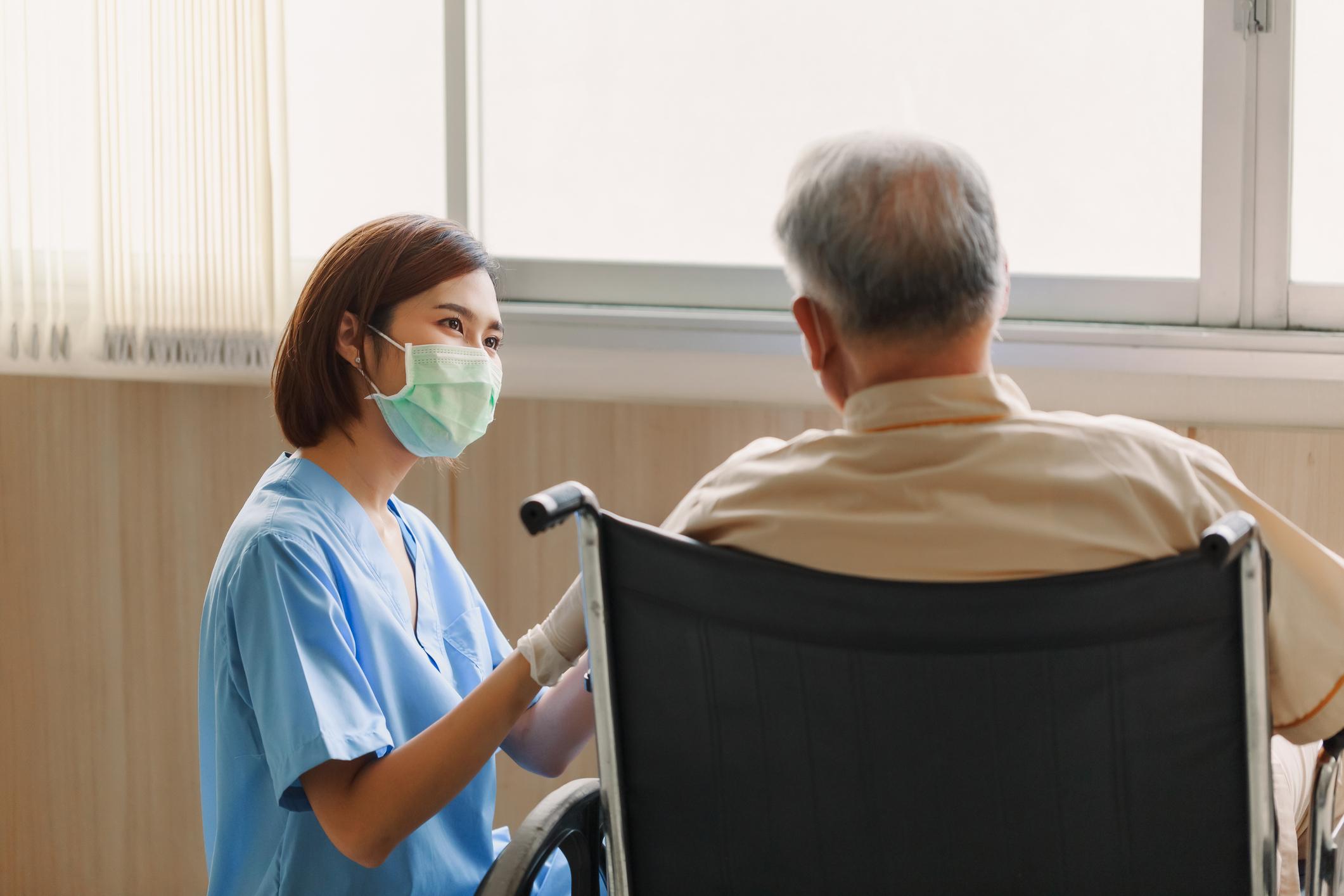 Young Asian woman nurse explaining information to elderly man patient in wheelchair 