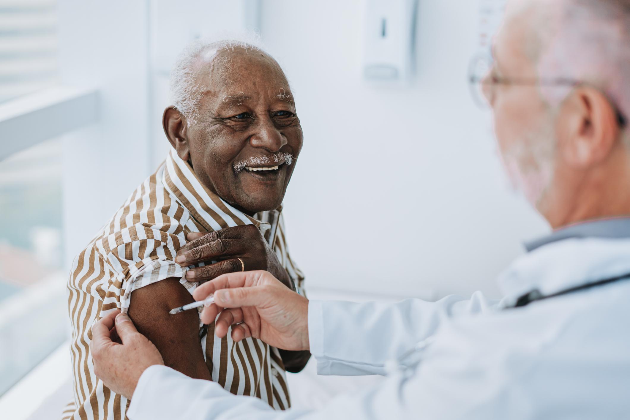 A doctor giving a vaccine to a smiling senior patient.