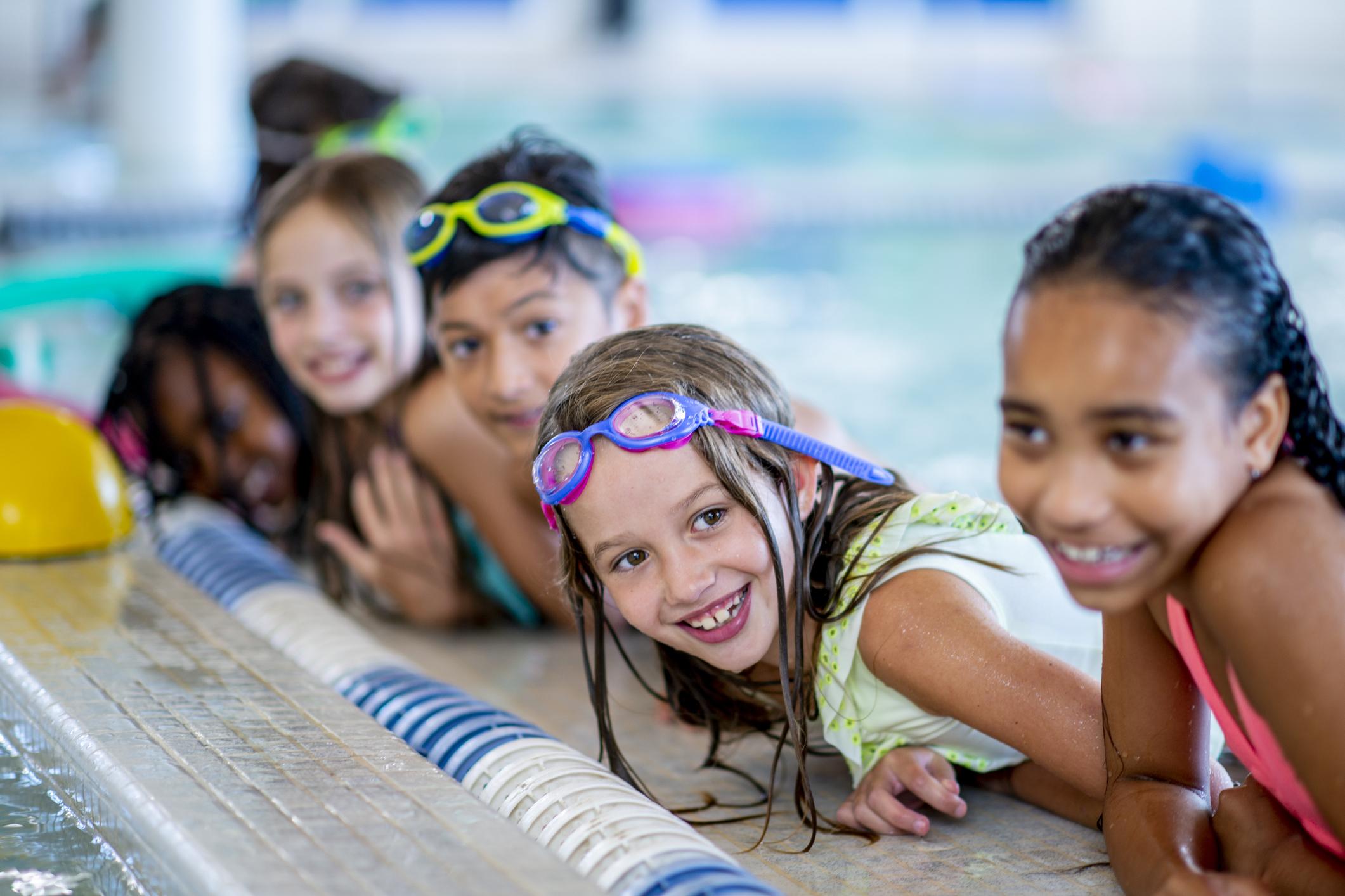 A multi-ethnic group of kids are indoors in a pool.