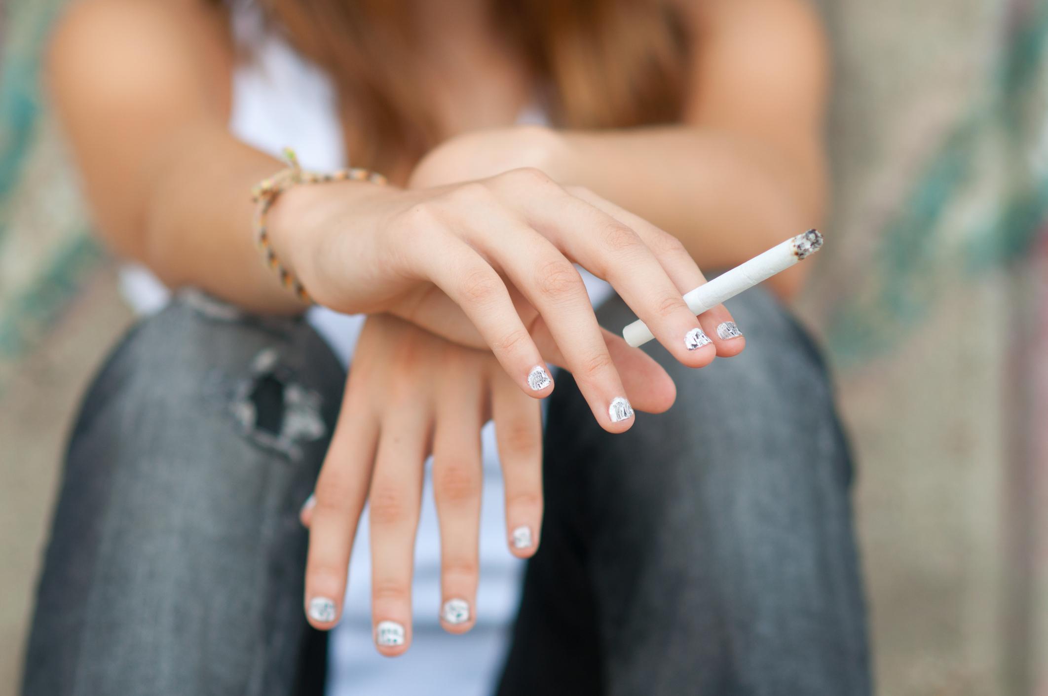 Teenage girl smoking cigarette while sitting on the street.