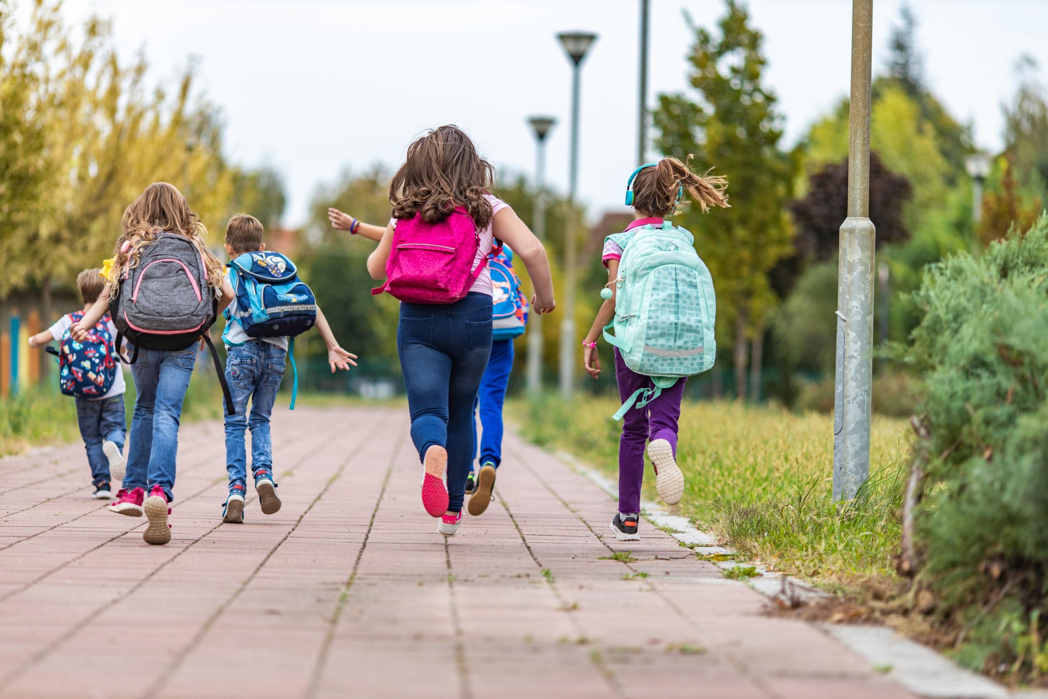 School children wearing backpacks running with their backs turned to the camera.