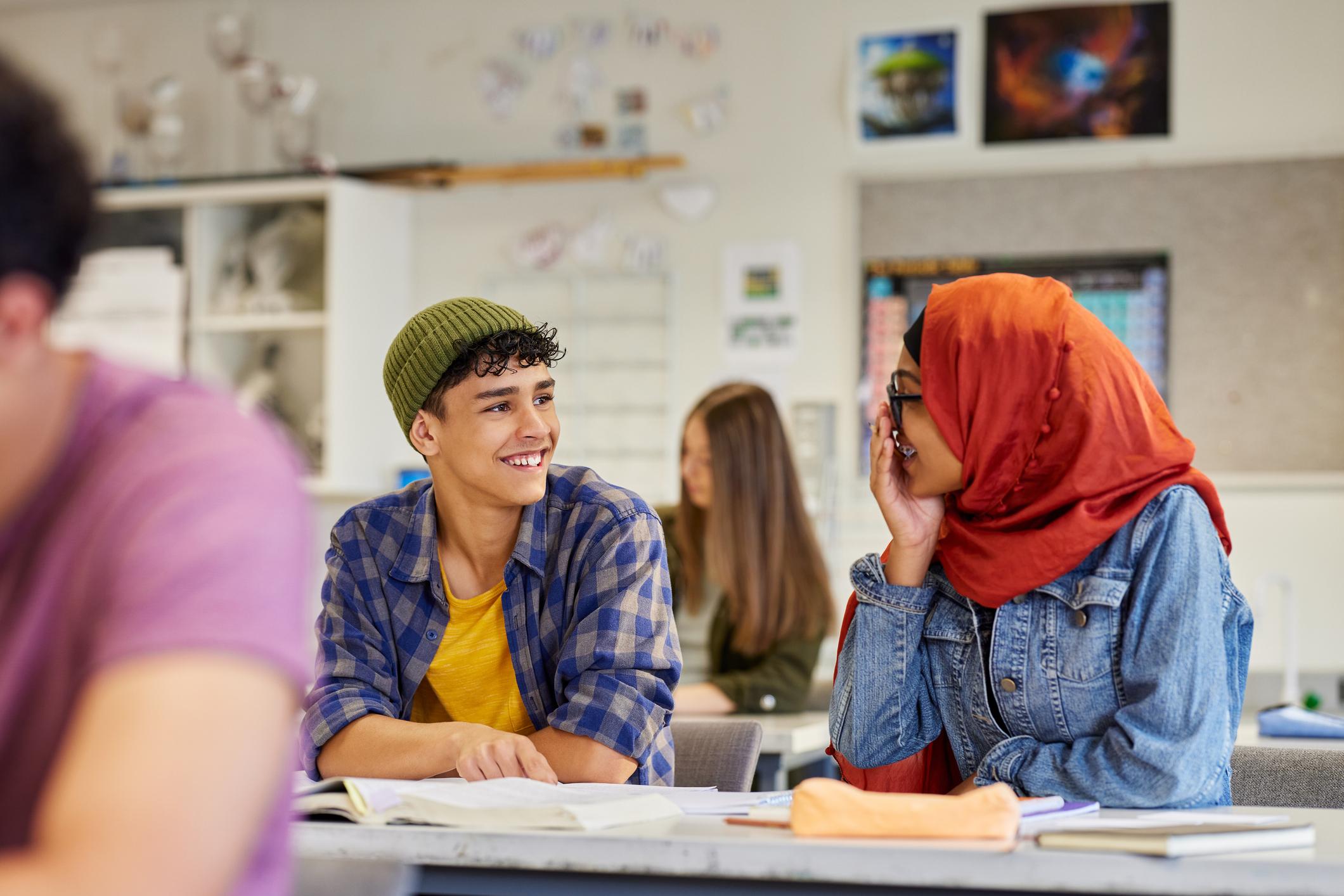 Two students smiling and talking happily during lesson at secondary school. 