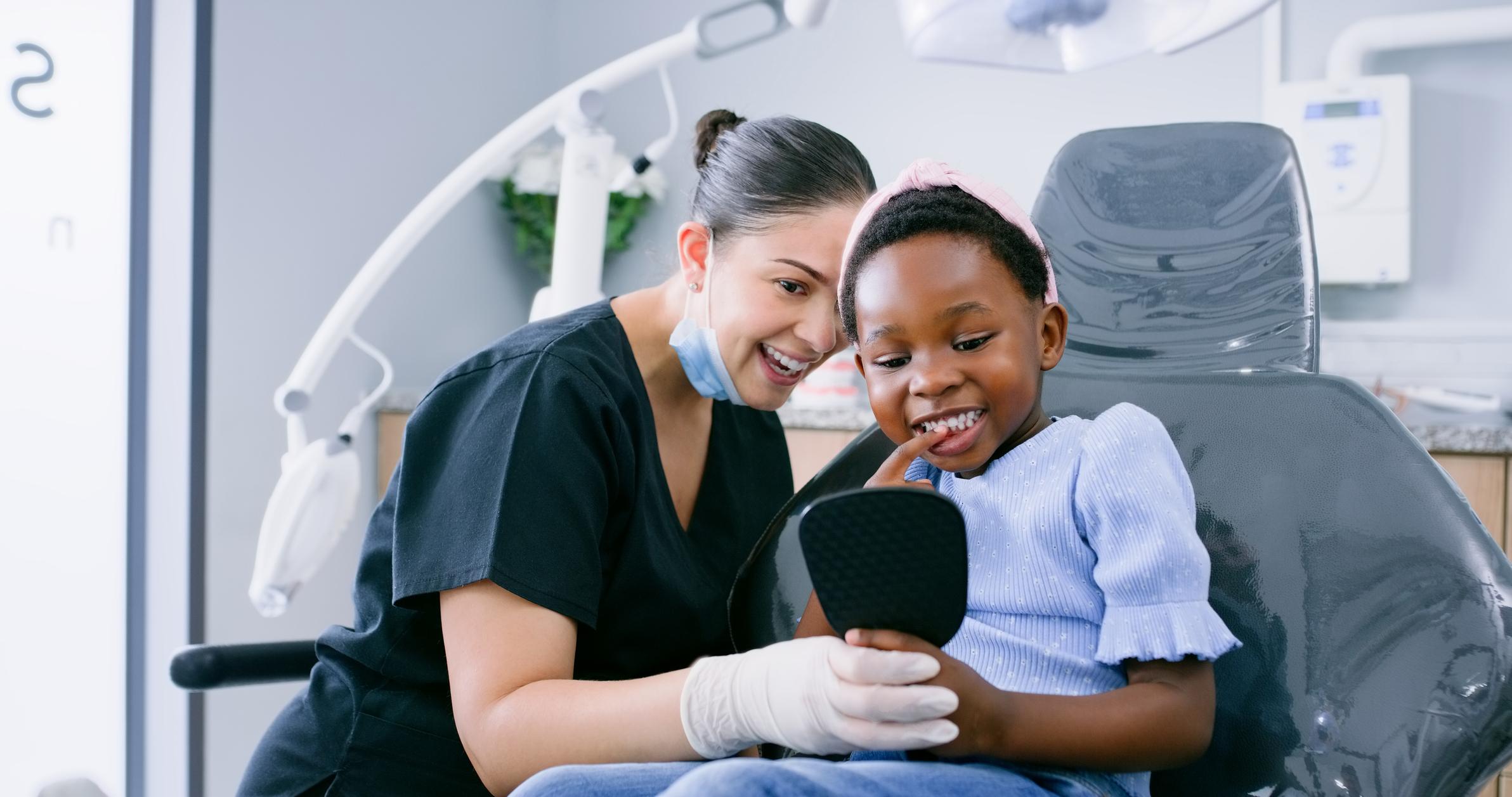 Dentist, child with mirror looking at her teeth while sitting in dental chair