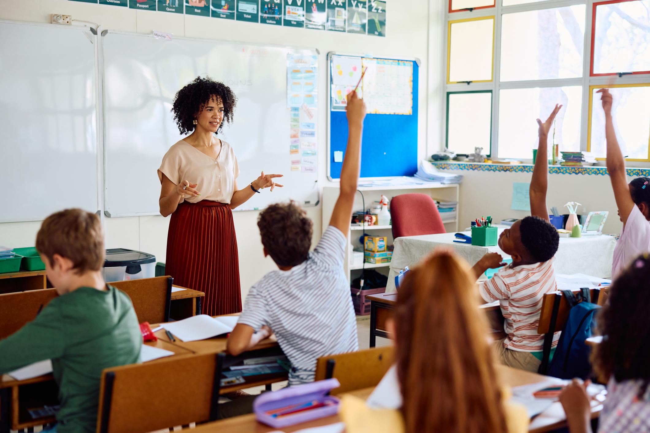 Elementary school teacher asking question, enthusiastic children with hands up 