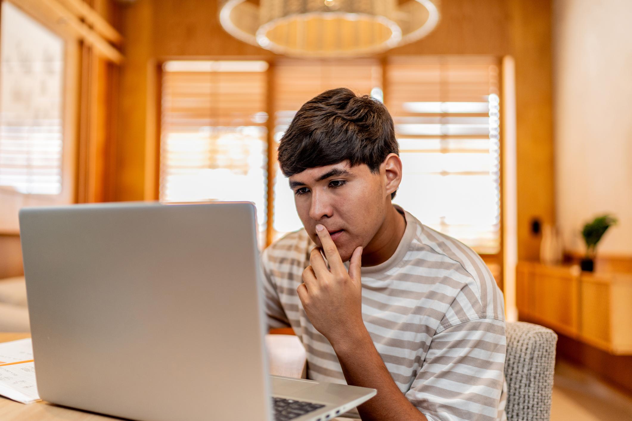 Teenage boy on laptop thinking
