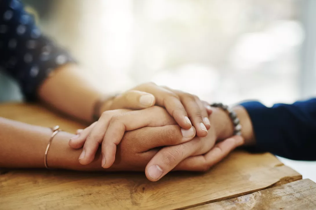 two people's hands shown on a table holding hands and providing comfort