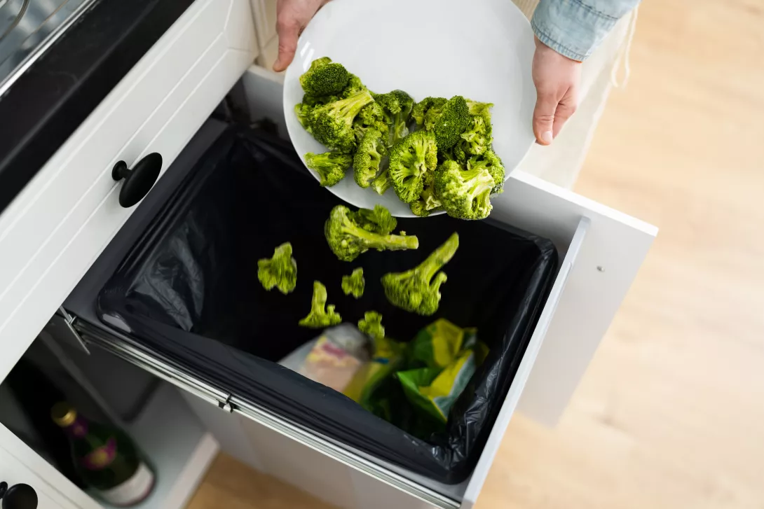 a plate of broccoli being scraped into the garbage