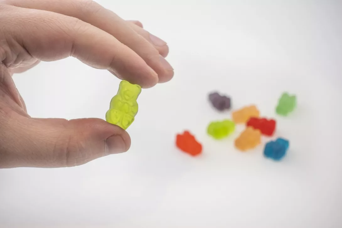 hand holding gummy bear candy with more candies sitting on the table behind