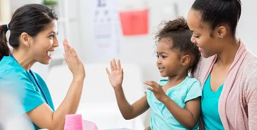 Vaccine success! A child giving a doctor a high five while sitting on her mom's lap