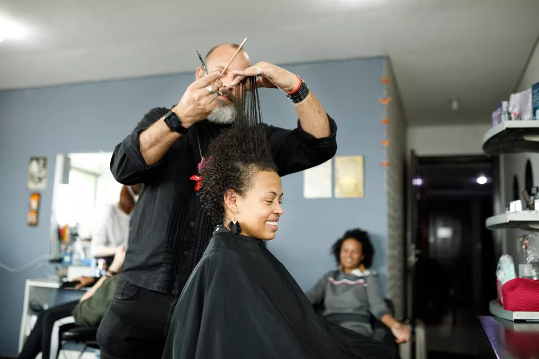 Male hairdresser combing hair up to do haircut for smiling woman