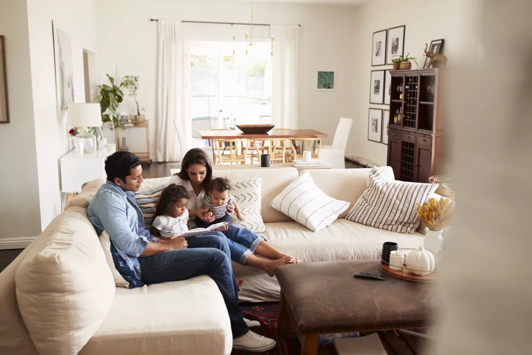  family sitting on sofa reading a book together in the living room, seen from doorway