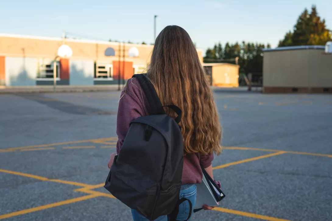 Teen girl in school parking lot, back of her